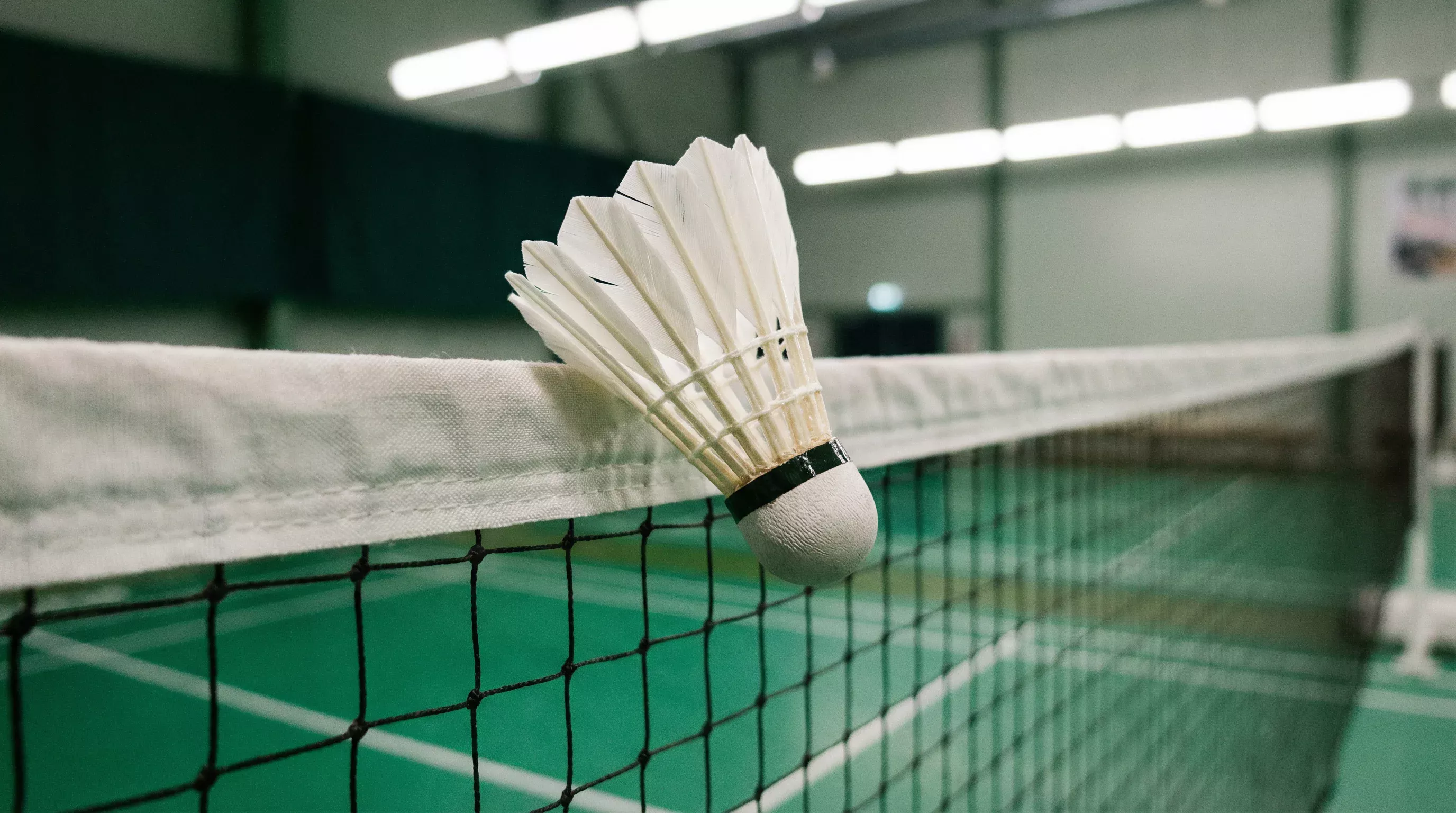 Badminton-Federball auf der Netzoberkante eines Hallenfelds mit Spielfeldlinien
