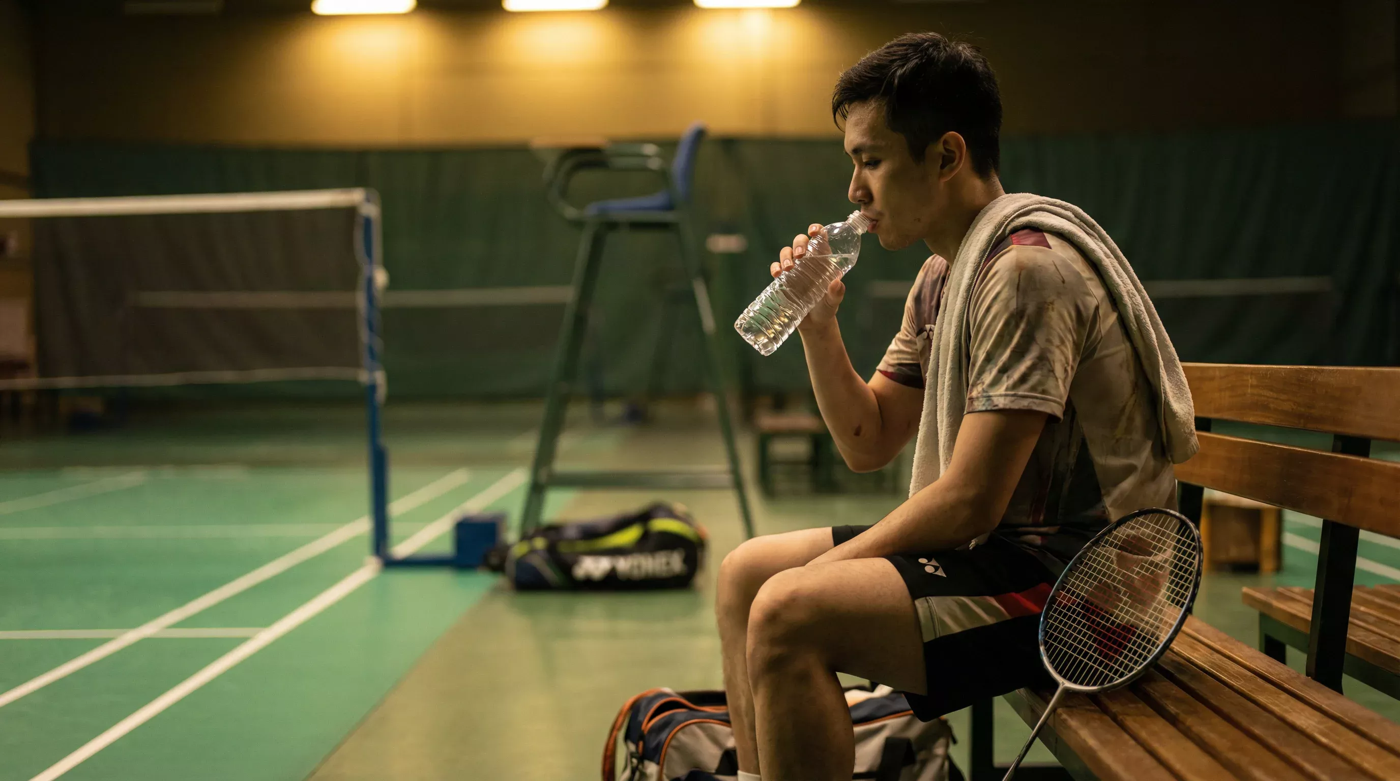 Badminton-Spieler trinkt Wasser während der Satzpause am Courtrand mit Handtuch