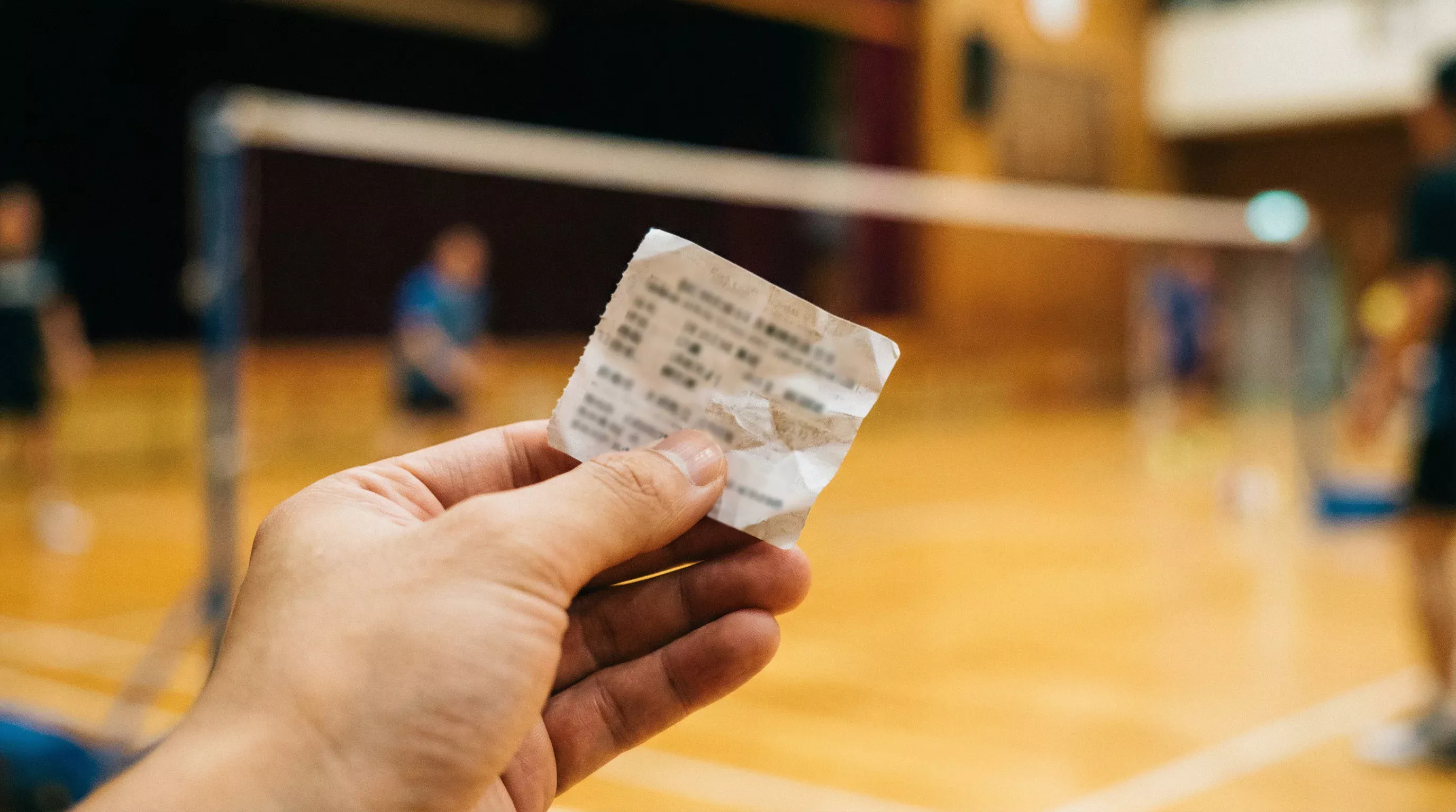 Nahaufnahme einer Hand, die einen Wettschein neben einem Badminton-Feld hält
